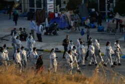 Greek officials wearing personal protective equipment arrive in an area where refugees and migrants from the destroyed Moria camp are sheltered on the island of Lesbos, Sept. 18, 2020.