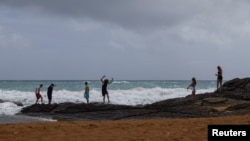 Los turistas caminan sobre una roca en una playa mientras la tormenta tropical Ernesto se acerca a Luquillo, Puerto Rico, 13 de agosto de 2024. 