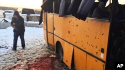 In this photo provided by the Ukrainian Interior Ministry, a man walks past snow covered with blood as he passes by a bus destroyed by a rebel shell at the checkpoint near the town of Volnovakha in the Donetsk region, eastern Ukraine, Jan. 13, 2015. 