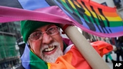 L'artiste Gilbert Baker, créateur du drapeau arc-en-ciel, porte une pancarte " Boycottons l'homophobie" lors de la parade pour la Saint Patrick à New York, le 17 mars 2014 