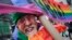 FILE - Artist Gilbert Baker, designer of the Rainbow Flag, is draped with the flag while holding a banner that reads "Boycott Homophobia" before the start of the St. Patrick's Day parade in New York City, March 17, 2014.