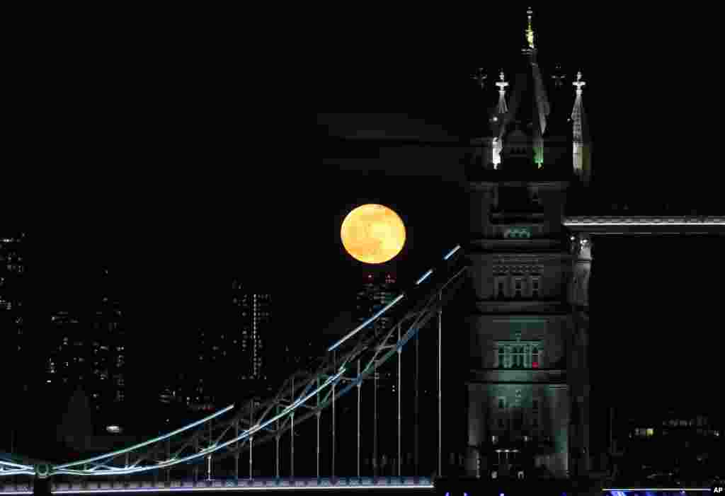 A full moon rises over the high buildings behind Tower Bridge in central London, March 29, 2021.