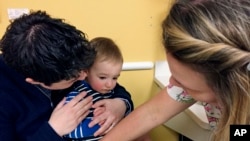 In this Tuesday, May, 2017, photo, 15-month-old August Goepferd received the measles, mumps and rubella booster shot at a clinic at Children's Minnesota in Minneapolis. Registered nurse Kim Flaata administered the shot. A Labor Department report says there will be lots of health care job openings in coming years. (AP Photo/Amy Forliti)