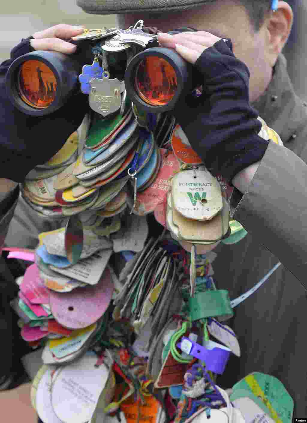 A racegoer looks through his binoculars covered with race passes at the Cheltenham Festival horse racing meet in Gloucestershire, western England. The four-day Cheltenham Festival is a highlight of the annual jump racing calendar.