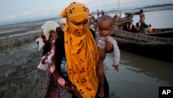 In this Sept. 21, 2017 photo, a Rohingya woman carries a child after crossing a stream on a small boat near Cox's Bazar's Dakhinpara area, Bangladesh. 