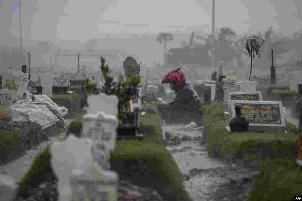 A man sits by the grave of a Covid-19 coronavirus victim amid pouring rain at Keputih cemetery in Surabaya, Indonesia.
