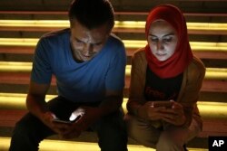 FILE - In this Aug. 1, 2016 file photo, Bahr Abdul Razzak, left, and his wife Noura Al-Ameer, use their smartphones in Istanbul.