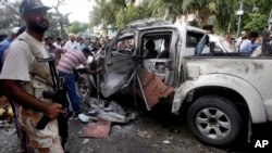 A Pakistani soldier stands next to a damaged vehicle at the site of suicide bombing in Karachi, Pakistan, July 10, 2013. A suicide bomber attacked a vehicle carrying one of the Pakistani president’s guards in the southern city of Karachi Wednesday, killing him and two others.