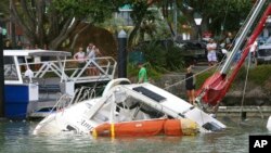 Orang-orang melihat kapal yang rusak di marina di Tutukaka, Selandia Baru, 16 Januari 2022, setelah gelombang dari letusan gunung berapi menyapu marina. (Foto: AP)