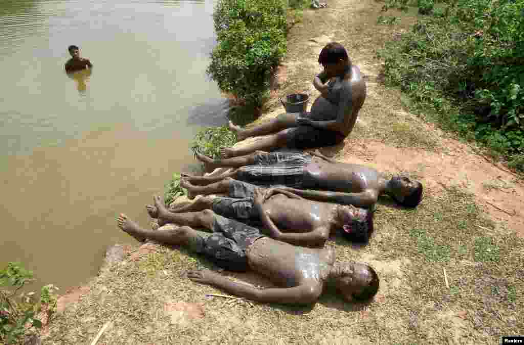 People relax after applying mud on their bodies to cool off on a hot summer day on the banks of the Kanchon Mala lake in the outskirt of Agartala, India.