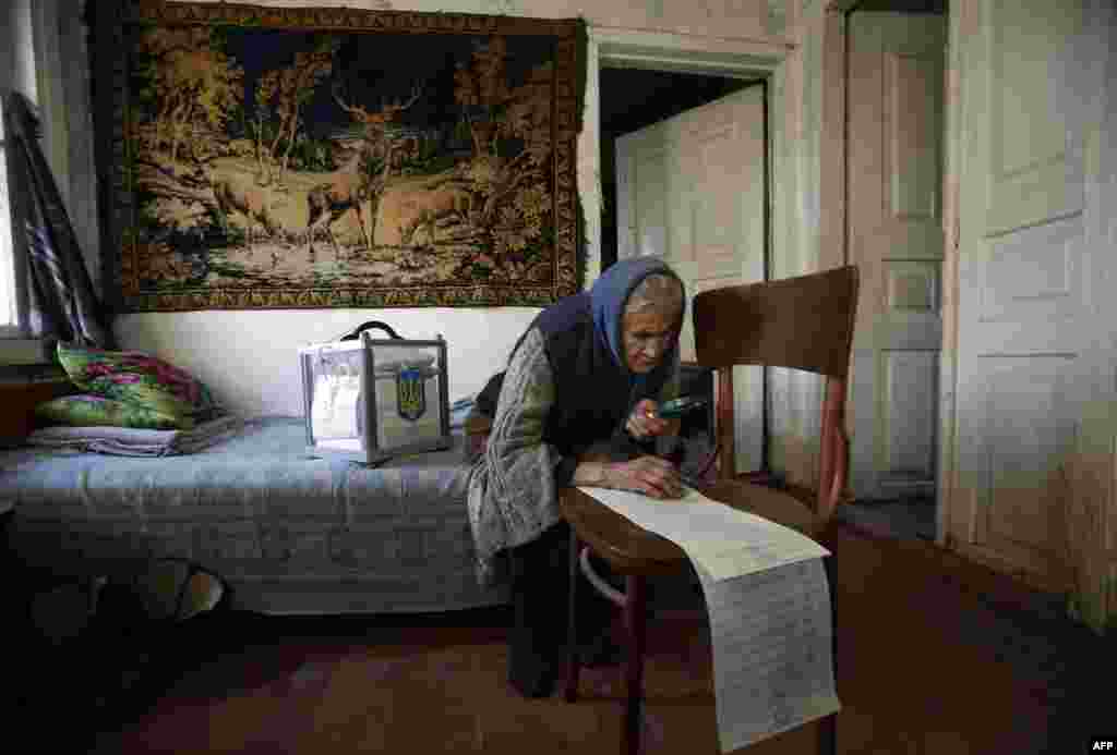 An woman uses a magnifying glass to read her ballot while voting at home in the village of Gornostaypol, some 80 km north of Kyiv during Ukraine's parliamentary elections.