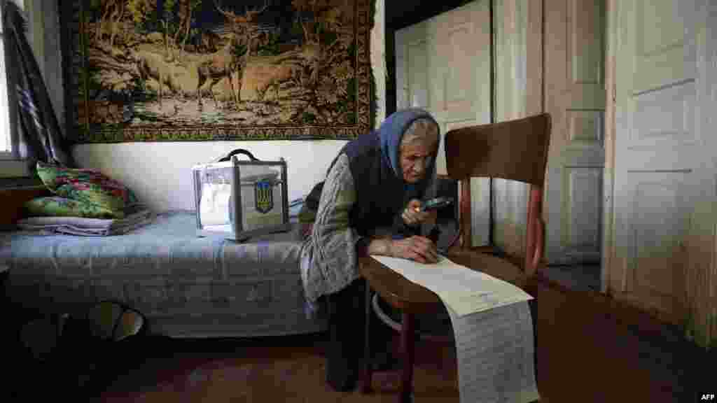 Une femme utilise une loupe pour lire son bulletin de vote tout en votant à la maison dans le village de Gornostaypol, quelques 80 kilomètres au nord de Kiev, le 26 Octobre 2014, lors des élections parlementaires en Ukraine. 