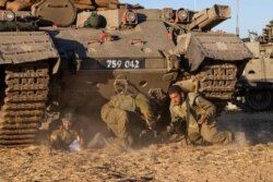 Israeli soldiers take cover under armored vehicles as a siren sounds warning of incoming rockets fired from the Gaza Strip in a staging ground near the Israeli-Gaza, May 15, 2021.