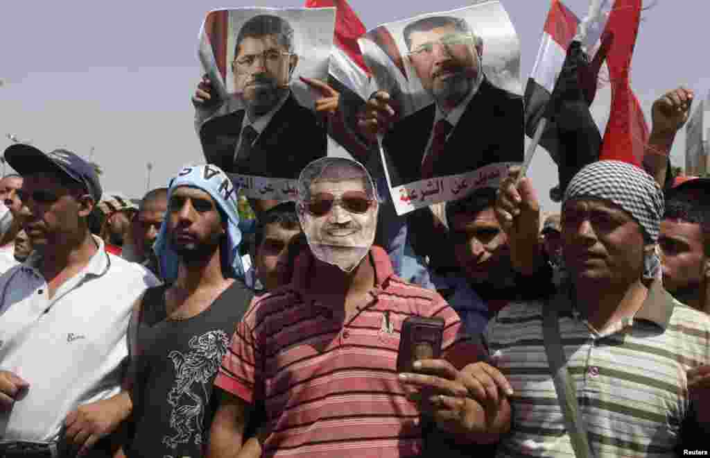 Seorang pendukung Mohamed Morsi memakai tepeng Morsi, saat para demonstran menyerukan slogan-slogan di luar markas tentara Republican Guard di Kairo (7/7). (Reuters/Asmaa Waguih)
