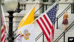 Dapro Vatikan an (drapo papal la) ap flote bò kote drapo ameriken an nan yon gran ri ki rele West Executive Avenue, tou prè La Mezon Blanch nan Washington, D.C. (Foto AP/Andrew Harnik, Lendi 21 septanm 2015).