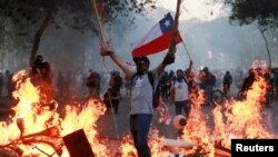 Un manifestante sostiene una bandera de Chile mientras está parado cerca de muebles en llamas durante una protesta contra el gobierno de Chile en Santiago, Chile, 18 de noviembre de 2019.