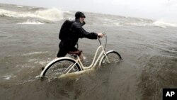 Tyler Holland guía su bicicleta a través del agua mientras los vientos de la tormenta tropical Barry empujan el agua desde el lago Pontchartrain hasta el dique el sábado 13 de julio de 2019, en Mandeville, La. (Foto AP / David J. Phillip)