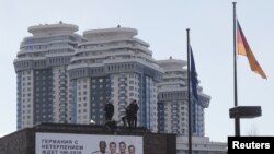 Para pekerja tampak berdiri di atas atap dari kantor kedutaan Jerman di Moskow, Rusia, saat berusaha membetulkan spanduk yang terpasang di gedung kantor tersbeut pada 29 Maret 2018. (Foto: Reuters/Maxim Shemetov)