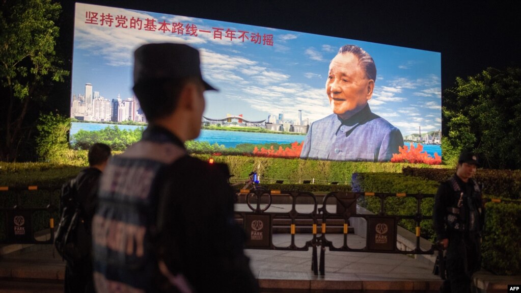 2018年12月17日，在中国深圳，保安人员站在中国已故最高领导人邓小平的宣传牌前面，牌子上写着“坚持党的基本路线一百年不动摇”。(photo:VOA)