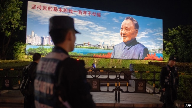 2018年12月17日，在中国深圳，保安人员站在中国已故最高领导人邓小平的宣传牌前面，牌子上写着“坚持党的基本路线一百年不动摇”。