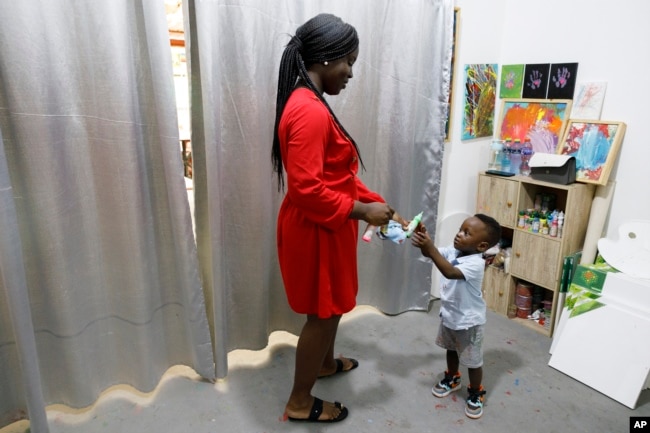 Chantelle Kuukua Eghan, 25, gives paint to her son Ace-Liam Nana Sam Ankrah, who will turn two in July, at her mother's art gallery in Accra, Ghana, Monday, May 27, 2024. (AP Photo/Misper Apawu)