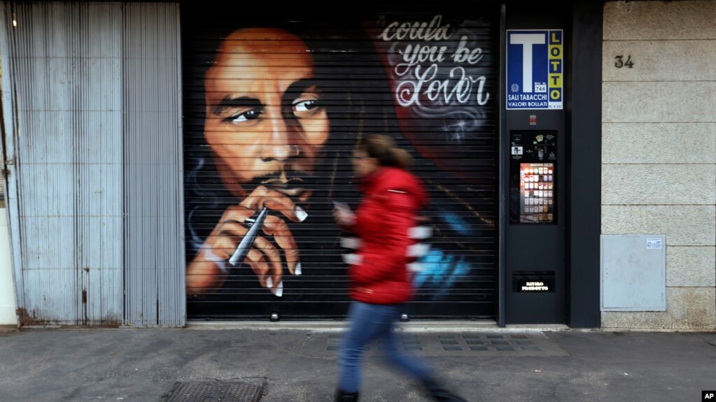 Una mujer pasa junto a un mural que muestra al ícono de la música reggae Bob Marley pintado en una tienda en Roma, Italia, el jueves 28 de noviembre de 2018.