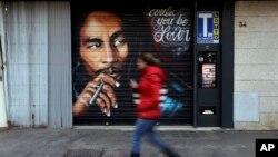 Una mujer pasa junto a un mural que muestra al ícono de la música reggae Bob Marley pintado en una tienda en Roma, Italia, el jueves 28 de noviembre de 2018.