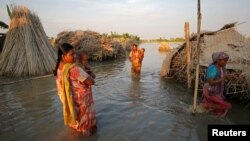 FILE - Women carry children as they make their way through a flooded area in Bogra, Bangladesh, Aug. 20, 2017. 