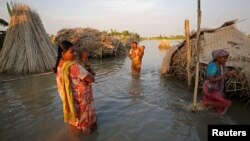 Women carry children as they make their way through a flooded area in Bogra, Bangladesh, Aug. 20, 2017. 