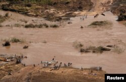 People stand on the banks where the bridge was washed away, in the aftermath of Cyclone Idai, near the village of John Segredo, Mozambique, March 24, 2019.