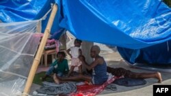 Seorang perempuan dan anak-anak beristirahat di tempat teduh di sebuah kamp untuk orang-orang yang kehilangan rumah saat gempa 14 Agustus di Les Cayes, Haiti, pada 23 Agustus 2021. (Foto: AFP)