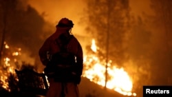 Un pompier regarde les flammes monter d'une colline en direction des maisons à l'ouest de Redding, en Californie, le 27 juillet 2018. 