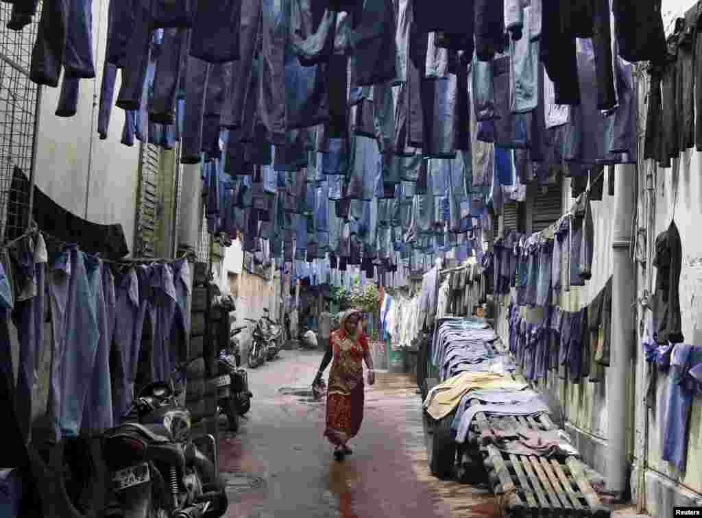 A woman walks through an alley amid used pairs of jeans hung to dry before they are sold in a second-hand clothes market in Kolkata, India.