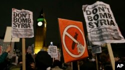 Protesters hold placards protesting a call for Britain to launch airstrikes on the Islamic State group inside Syria, during a demonstration outside Parliament ahead of a vote in London, Dec. 2, 2015.