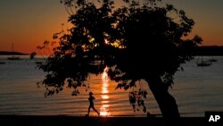 FILE - A runner gets in her exercise at dawn on Willard Beach in South Portland, Maine, Sept. 13, 2017.