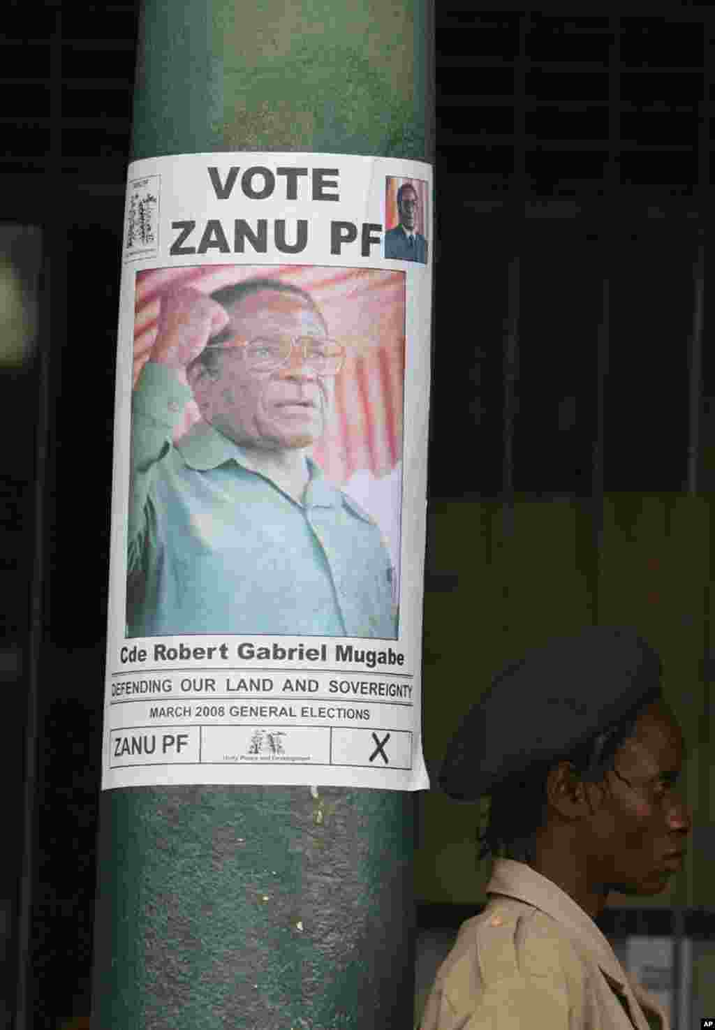 A security guard stands next to a President Robert Mugabe campaign poster in Harare, Zimbabwe, Tuesday, February, 26, 2008.