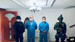 In this photo released by Colombia's Prosecutor's Press Office, a police officer and a soldier flank Mark Grennon, second left, and his son Joseph Grennon during a raid in Santa Marta, Colombia, Aug. 11, 2020.