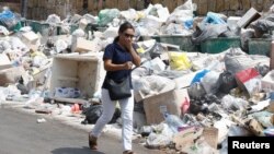 A woman covers her nose as she walks past garbage piled up along a street in Dekwaneh area, Mount Lebanon, Aug. 29, 2016. 