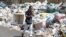 A woman covers her nose as she walks past garbage piled up along a street in Dekwaneh area, Mount Lebanon, Aug. 29, 2016. 