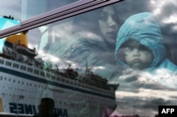 FILE - A woman and a child peer from a bus, after migrants and refugees disembarked from a government chartered ferry, seen in reflection, in the port of Piraeus in Athens on Nov. 27, 2015.