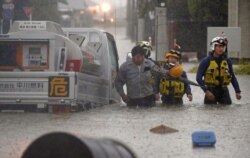 Seorang pria diselamatkan oleh polisi saat mobilnya terjebak di jalanan yang banjir yang dipicu oleh hujan lebat di Omuta, prefektur Fukuoka, Jepang selatan 7 Juli 2020 dalam foto yang diambil oleh Kyodo, Jepang. (Foto: Kyodo / via REUTERS)