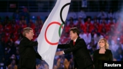 International Olympic Committee (IOC) President Thomas Bach (L) passes the Olympic flag to PyeongChang Mayor Lee Sok-ra (2nd R) during the closing ceremony for the Sochi 2014 Winter Olympics, Feb. 23, 2014.