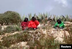 FILE - Migrants sit outside the immigration center on the southern Italian island of Lampedusa Feb. 19, 2015.