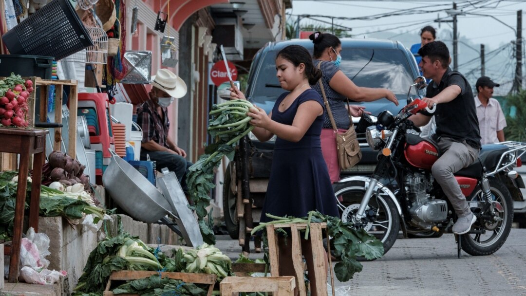 A girl cuts vegetables outside a store as other residents chat in El Paraiso, Honduras July 24, 2021.