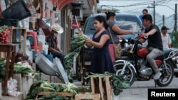 A girl cuts vegetables outside a store as other residents chat in El Paraiso, Honduras July 24, 2021.