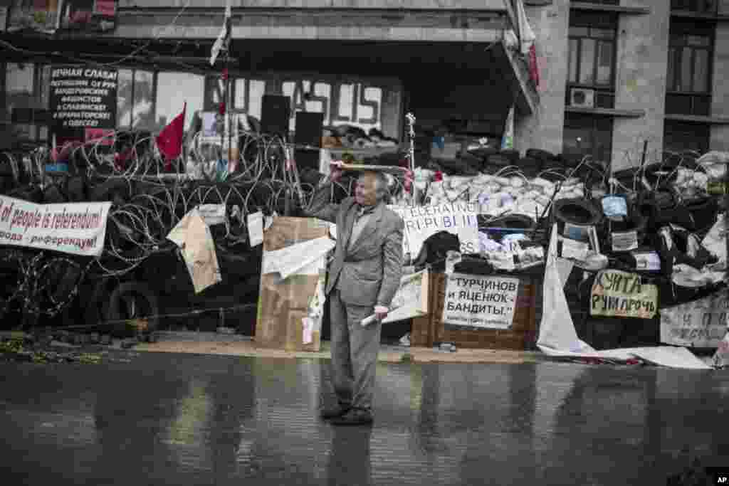 A pro-Russia man takes cover from the rain with a piece of wood at the barricades surrounding the Donetsk administration building after a press conference to inform the media about a referendum, May 8, 2014.