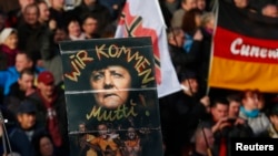 Supporters of the anti-Islam movement Pegida hold a poster depicting German Chancellor Angela Merkel with text reading "We are coming, mommy!" during a demonstration in Dresden, Germany, Feb. 6, 2016.