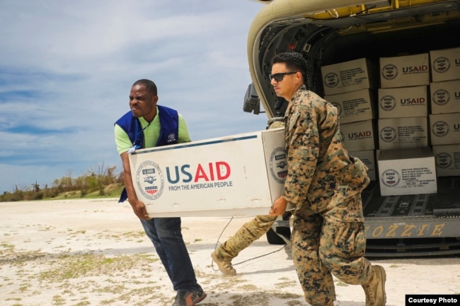 FILE - Cpl. Steven Arroyo, a heavy equipment mechanic with Marine Wing Support Detachment 31, aids an International Organization for Migration representative in carrying supplies at Jeremie, Haiti, Oct. 9, 2016. (U.S. Marine Corps photo by Cpl. Samuel Guerra/Released)