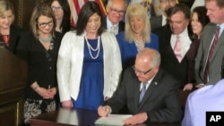 Jenny Teeson, center, of Andover, Minnesota, looks on as Minnesota Gov. Tim Walz signs a bill at the Capitol in St. Paul, May 2, 2019, repealing a Minnesota law that prevented prosecutors from filing sexual assault charges against people accused of raping their spouse.