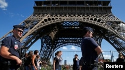 FILE - French CRS policemen patrol as tourists walk past in front of the Eiffel Tower in Paris, Aug. 20, 2016. 